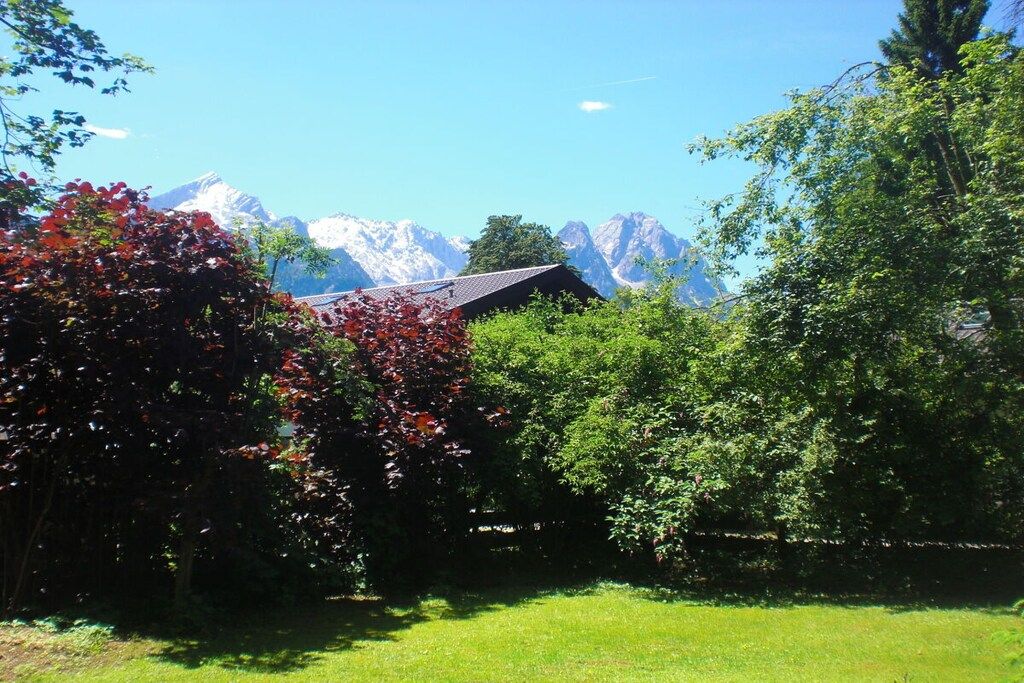 A house with a mountain backdrop, surrounded by lush greenery.