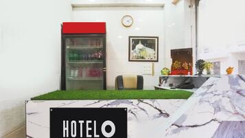 Zona de recepción de un hotel con mostrador, un reloj, un refrigerador y un cuadro en la pared.