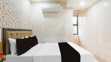 Une chambre d’hôtel avec un lit, une tête de lit, un climatiseur fixé au mur et une fenêtre.