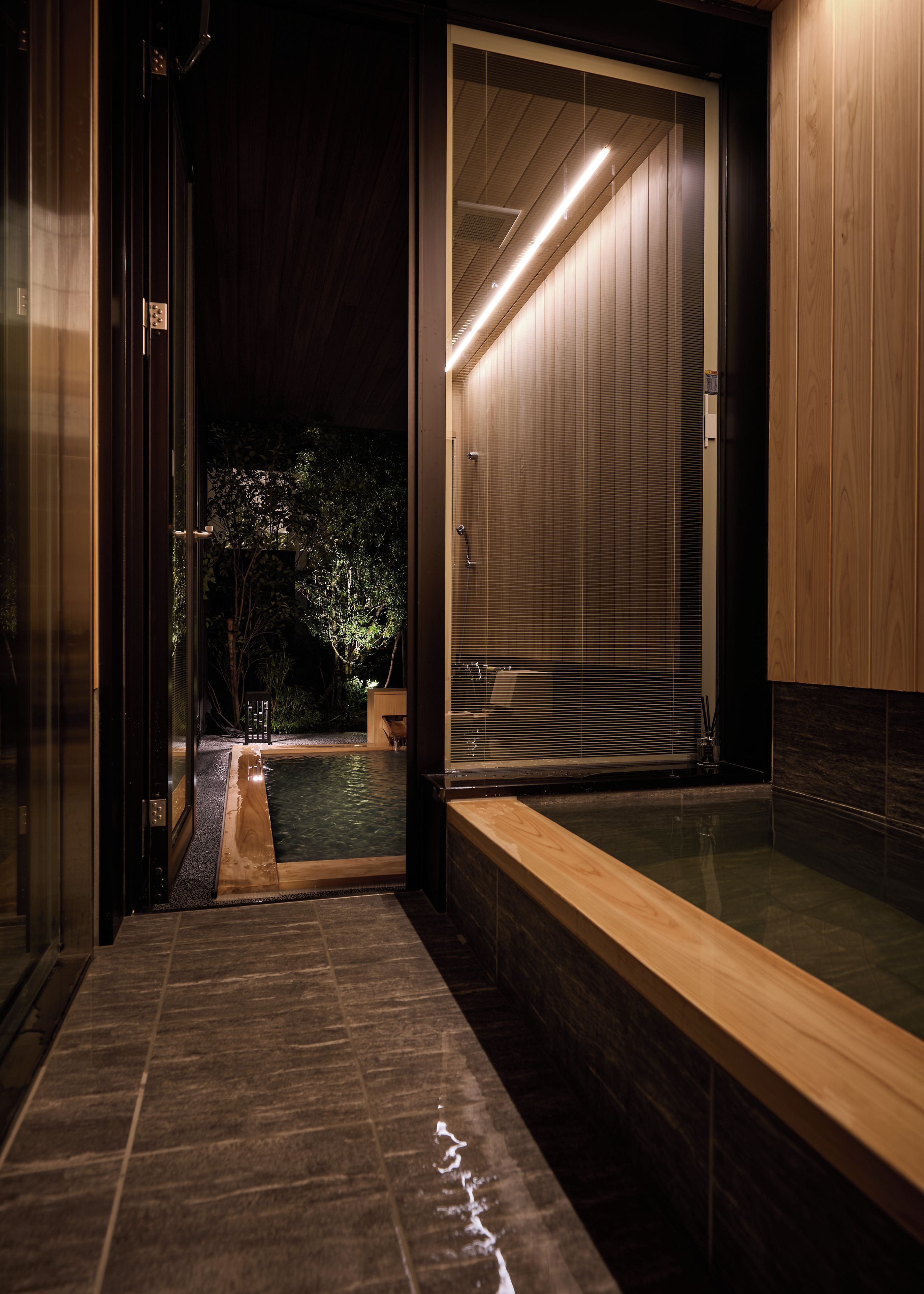 Un baño moderno con una puerta de vidrio que da a un área de piscina, un banco de madera y una bañera grande.