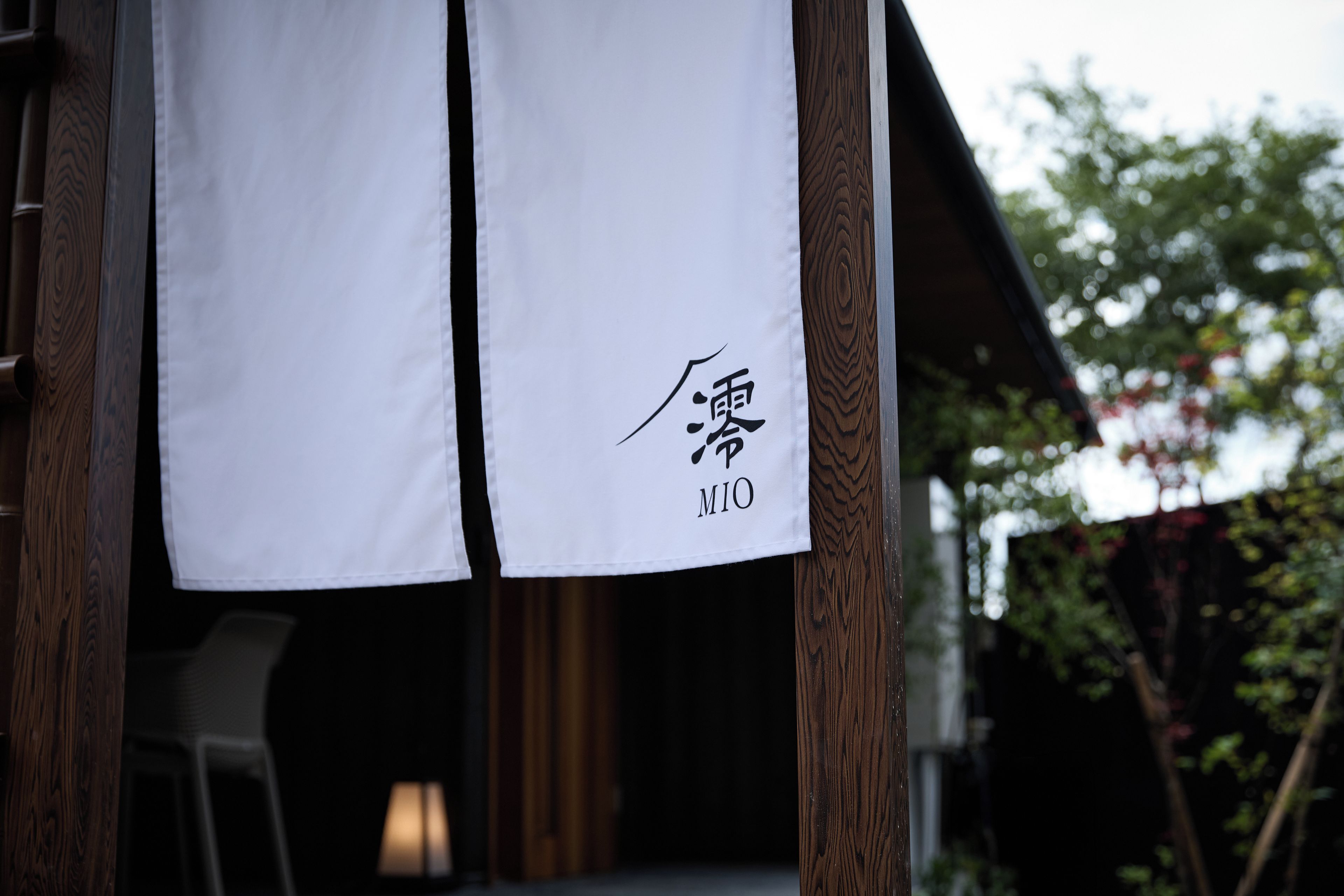 A white cloth with Japanese characters and the word 'MIO' hanging on a wooden structure.