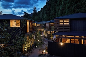 A row of traditional wooden buildings with large windows, surrounded by a garden with rocks and plants, under a twilight sky. - tuuli YUFU Kinrinko (Yufu)