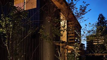 Un edificio de madera con techo inclinado, una ventana visible y un camino que lleva a una entrada con portón.
