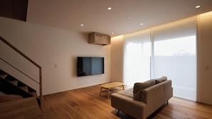 A modern living room with a sofa, a flat-screen TV mounted on the wall, a small table, and a staircase leading to an upper level. - tuuli YUFU Kinrinko (Yufu)