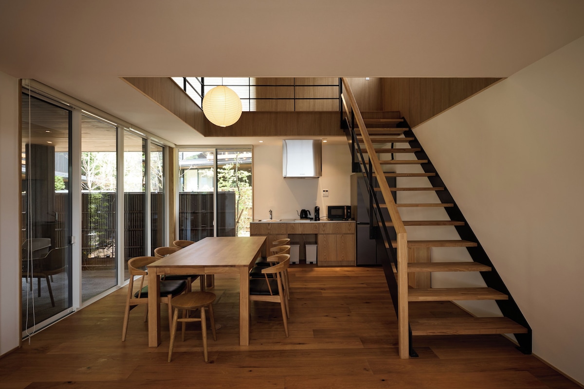 Un interior moderno con comedor, cocina y una escalera de madera.