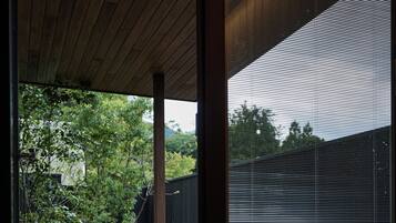 Una habitación tradicional japonesa con techo de madera, suelo de esteras de tatami, un pequeño banco de madera y una ventana con vistas a un jardín.