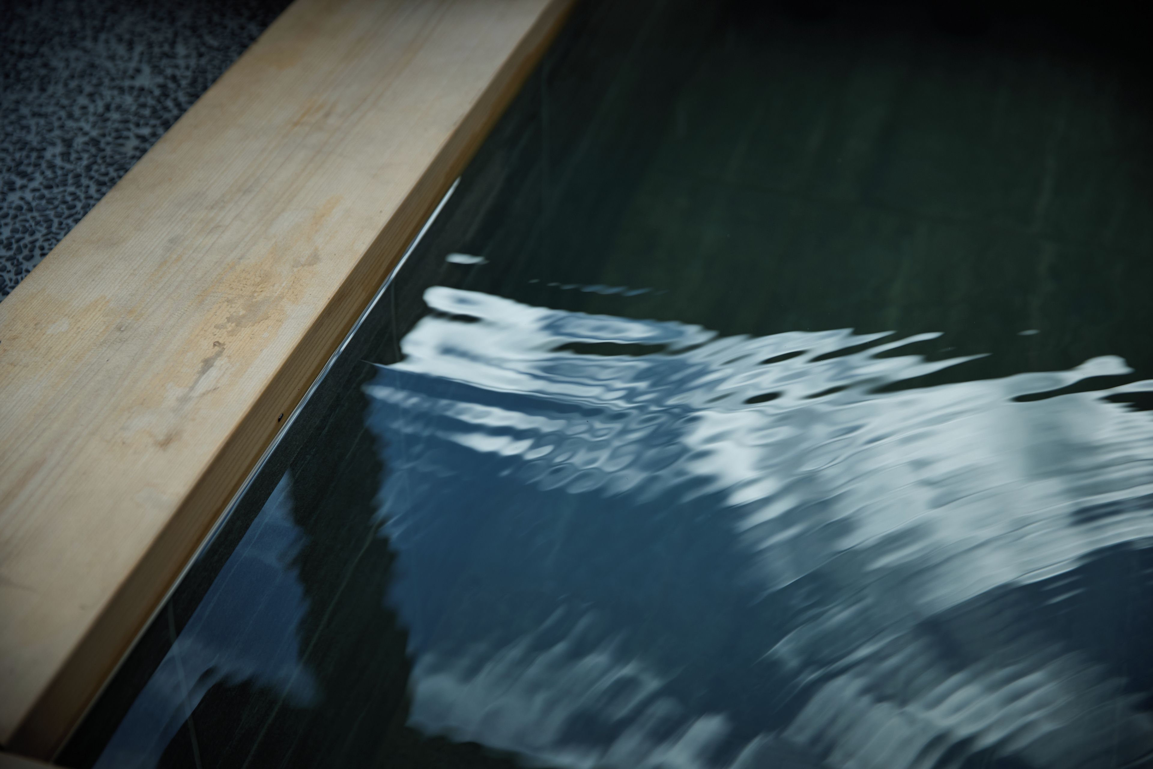 Ein hölzerner Poolrand mit einer dunklen, spiegelnden Oberfläche.