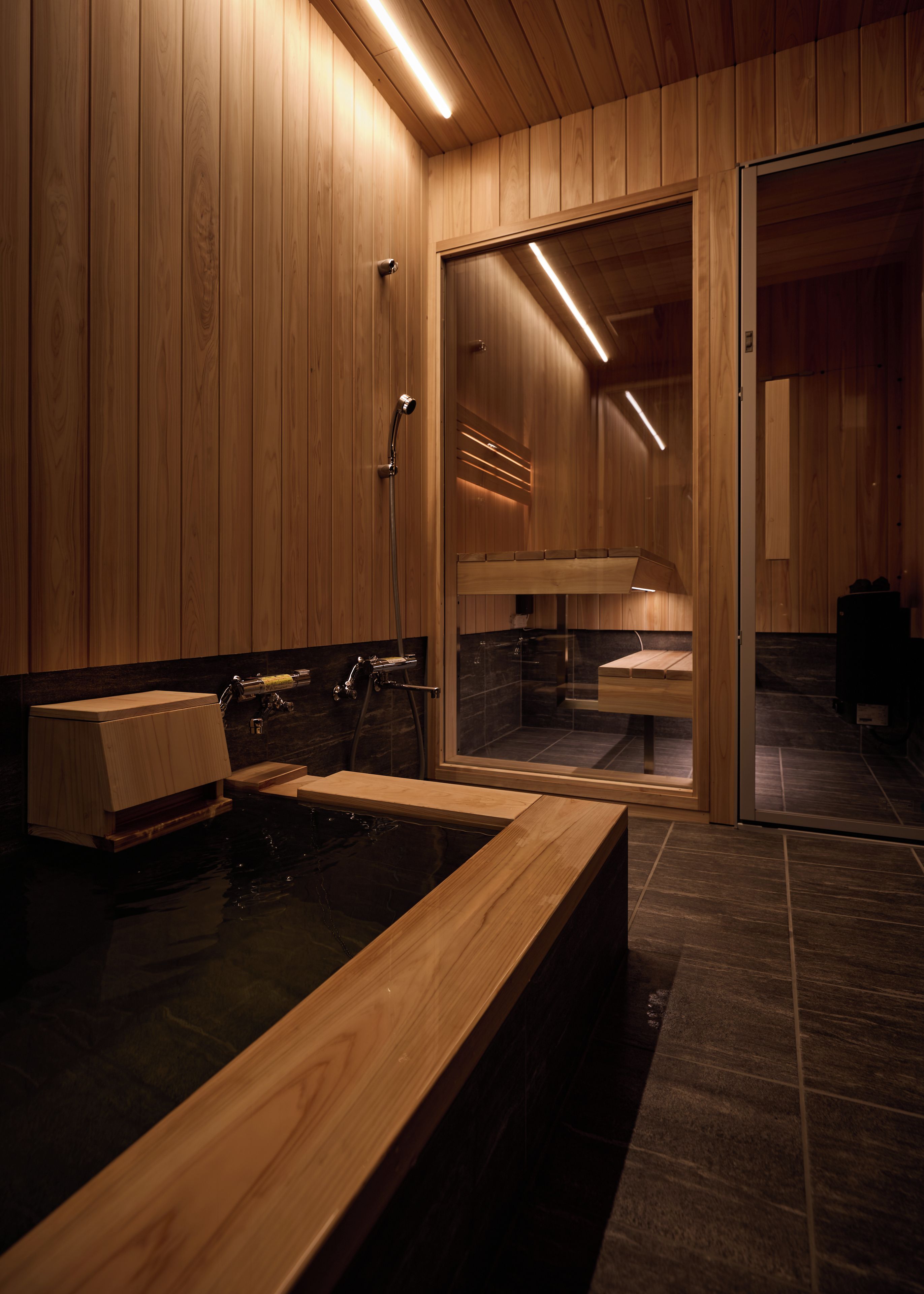 Un interior de madera con una bañera, una ducha y un vidrio que da a otra habitación.