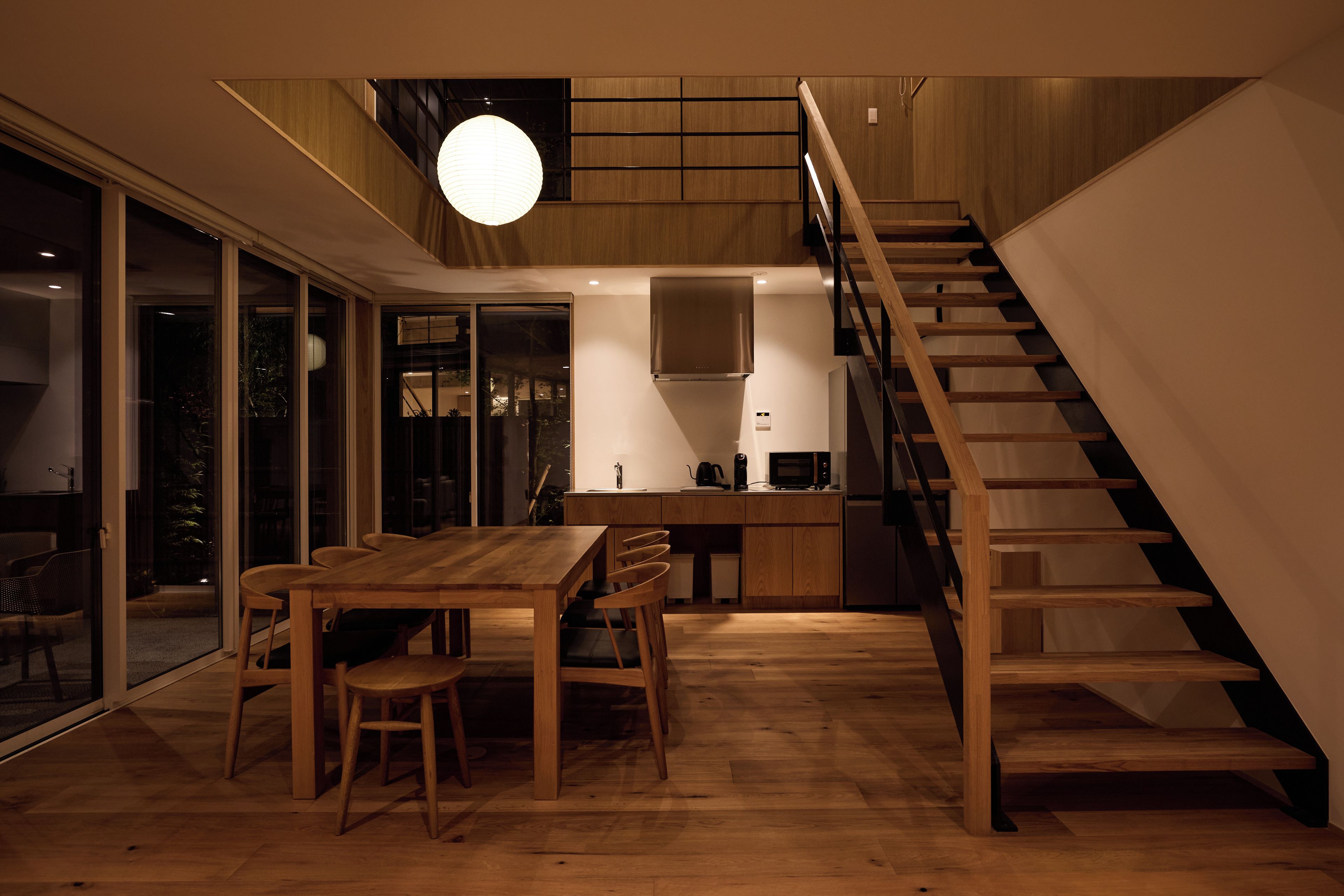 Een moderne keuken met een houten trap, een zithoek met stoelen en een groot raam.