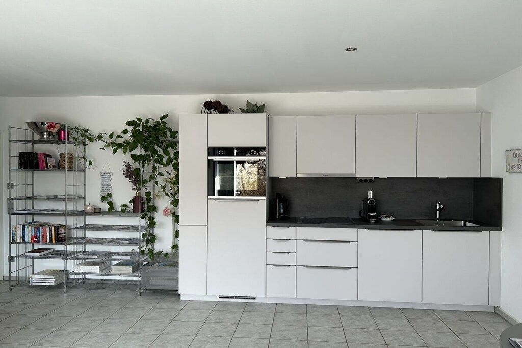 A modern kitchen with white cabinetry, a black countertop, and a built-in oven.