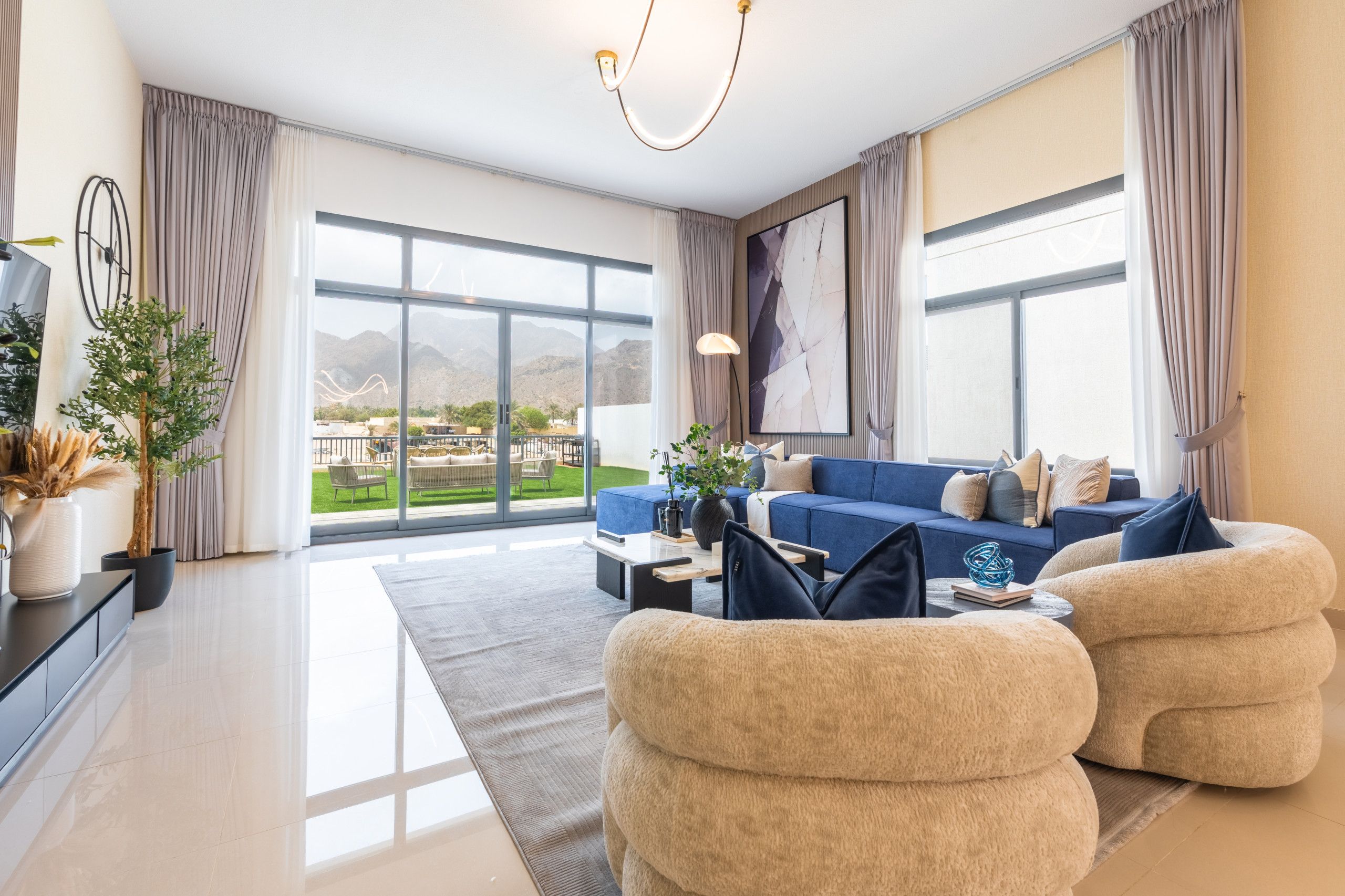 Ein modernes Wohnzimmer mit einer Couch, Sesseln, einem Couchtisch und Blick auf eine gebirgige Landschaft durch große Fenster.