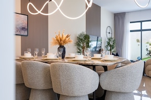 Un comedor moderno con una mesa de mármol, sillas tapizadas y un jarrón con plantas secas.