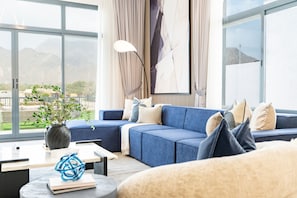Una sala de estar moderna con un sofá azul, una mesa de centro y un amplio ventanal con vistas al exterior.