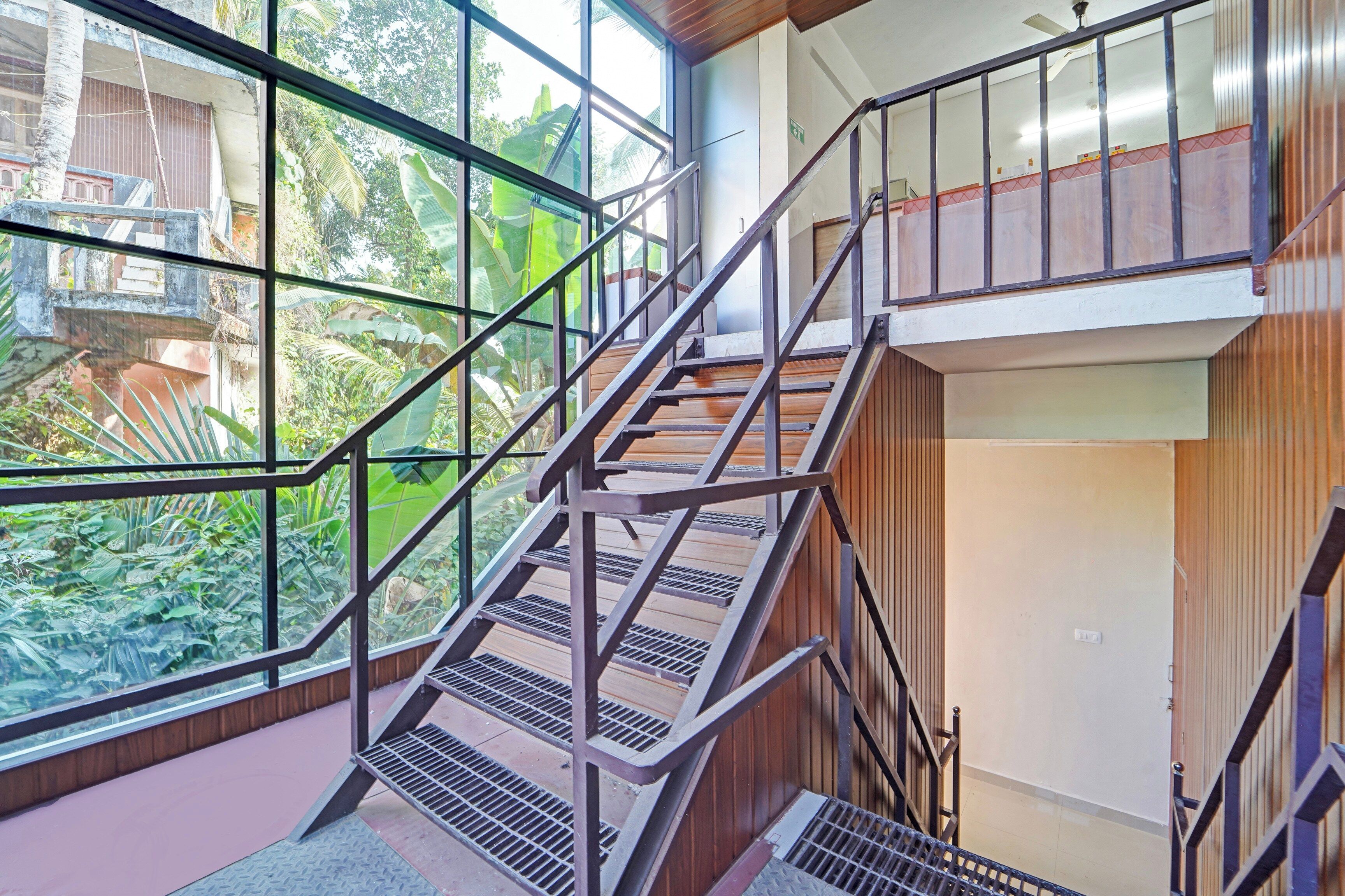 Un interior de varios niveles con una escalera, ventanas amplias y vistas al exterior con vegetación.
