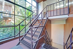 Un interior de varios niveles con una escalera, ventanas amplias y vistas al exterior con vegetación.
