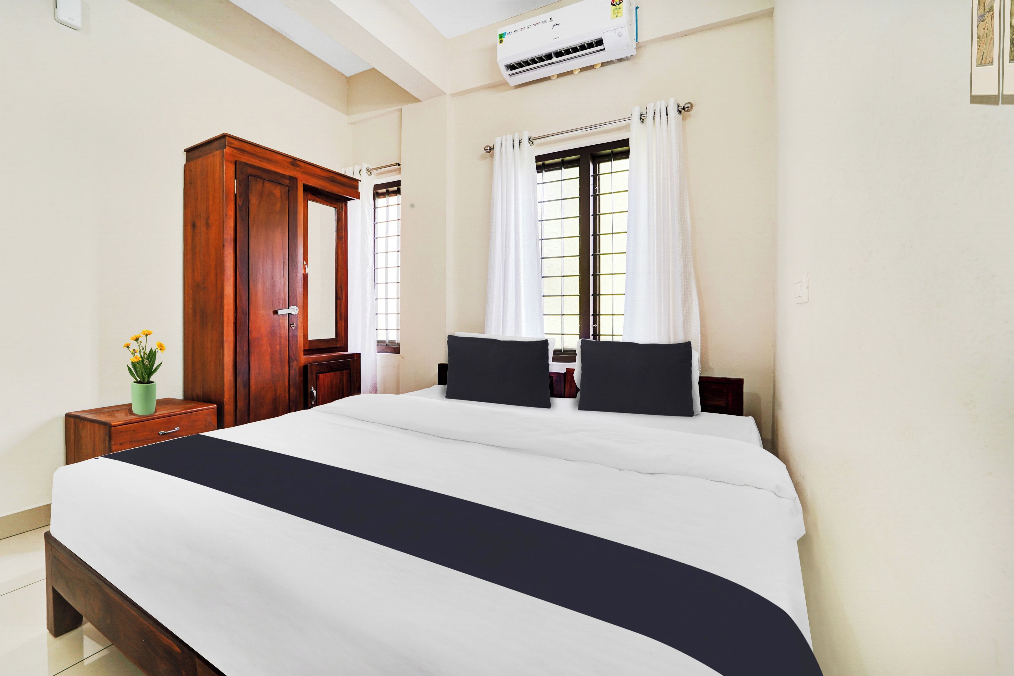 Un dormitorio con una cama grande, un armario de madera, una mesita de noche con una planta y una ventana con cortinas.
