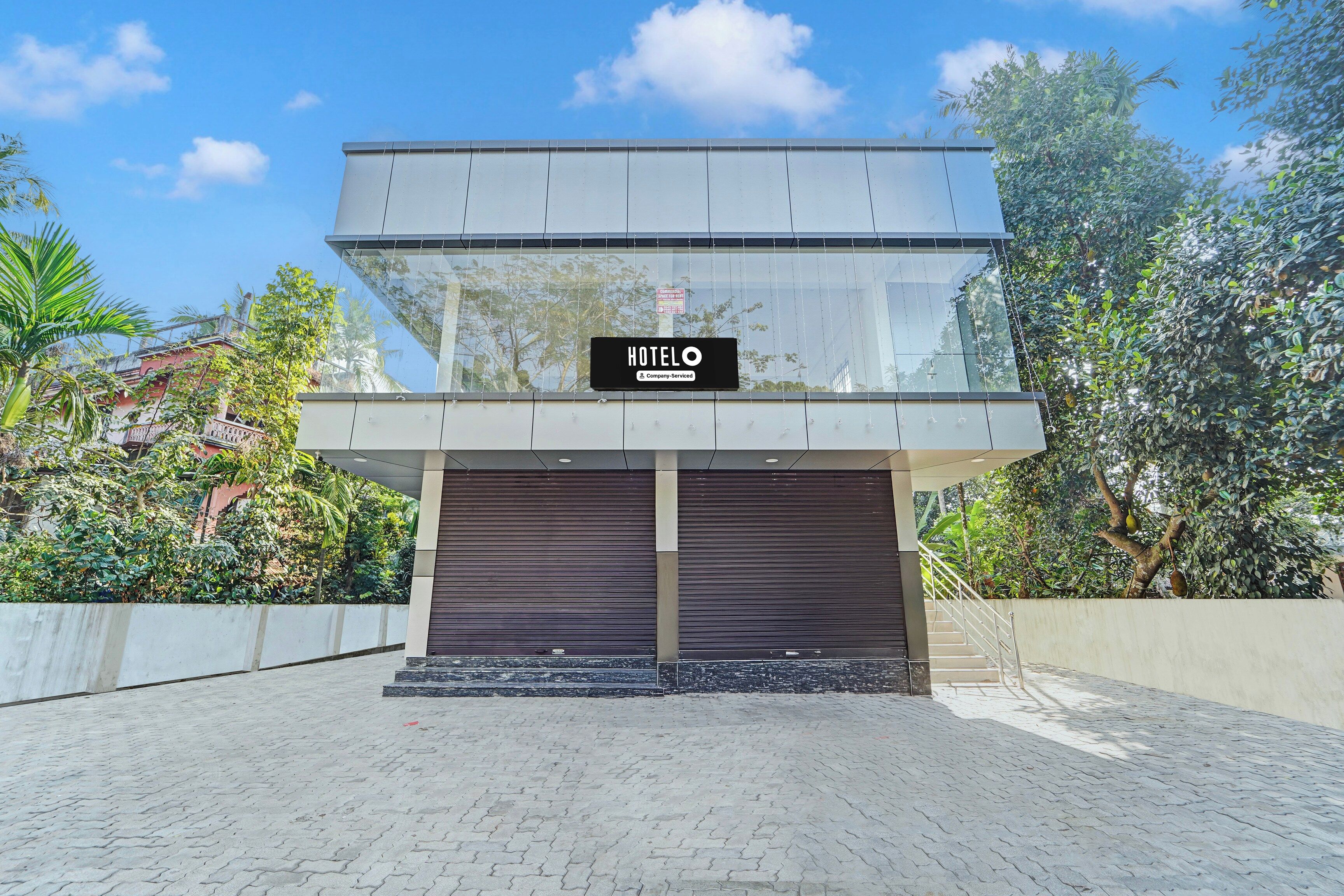 A modern hotel with a glass facade, a sign indicating it's a company-serviced hotel, and a gated entrance.