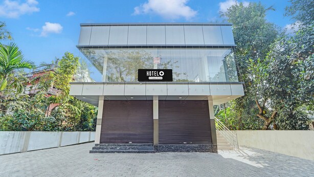 A modern hotel with a glass facade, a sign indicating it's a company-serviced hotel, and a gated entrance.