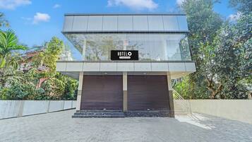 A modern hotel with a glass facade, a sign indicating it's a company-serviced hotel, and a gated entrance.