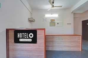 Un mostrador de recepción de hotel con un letrero que indica servicio de empresa. Hay un ventilador de techo y una lámpara fijada a la pared sobre el mostrador.