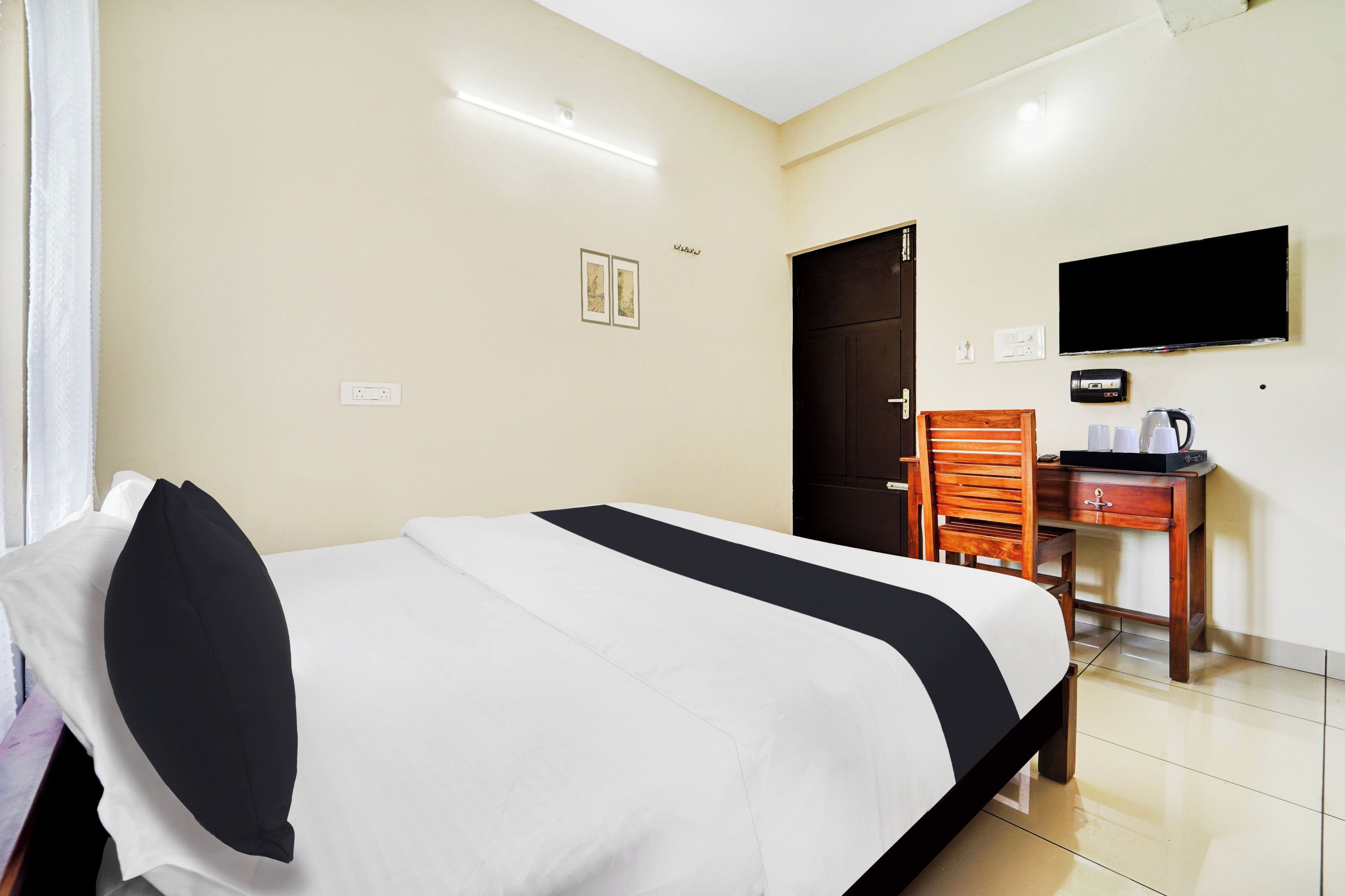 A hotel room with a bed, a desk with a chair, a television, and a door.