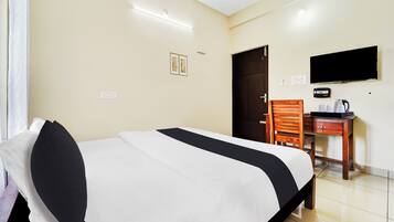 A hotel room with a bed, a desk with a chair, a television, and a door.