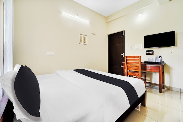 Una habitación de hotel con una cama, un escritorio con una silla, un televisor y una puerta.