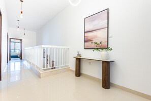 Ein modernes Interieur mit einer weißen Geländer, einem Konsolentisch mit Vase und Pflanze sowie einem großen abstrakten Gemälde an der Wand.