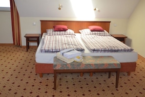 A double bed with a wooden headboard, two bedside tables, a bench with towels, and a patterned carpet. - Balmer See with direct lake view (Balm\/Usedom)