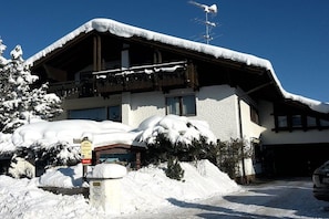 Un edificio cubierto de nieve con un balcón, un letrero que indica un restaurante y un coche estacionado al frente.