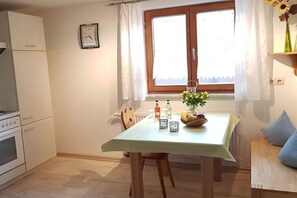 Uma cozinha com mesa de jantar, cadeiras, relógio e janela com cortinas.