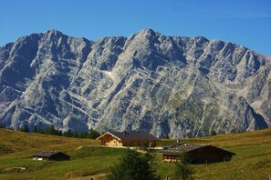 A mountain cabin with a sloped roof, surrounded by a grassy landscape and a large mountain in the background. - Holiday apartment with 3 bedrooms (Schönau am Königssee)