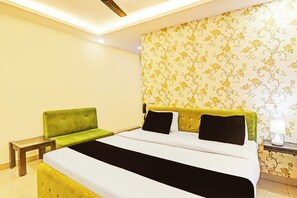 A hotel room with a bed, a green armchair, a bedside table, and a lamp. - Super Hotel O Kathauta Jheel Malhaur (Lucknow)
