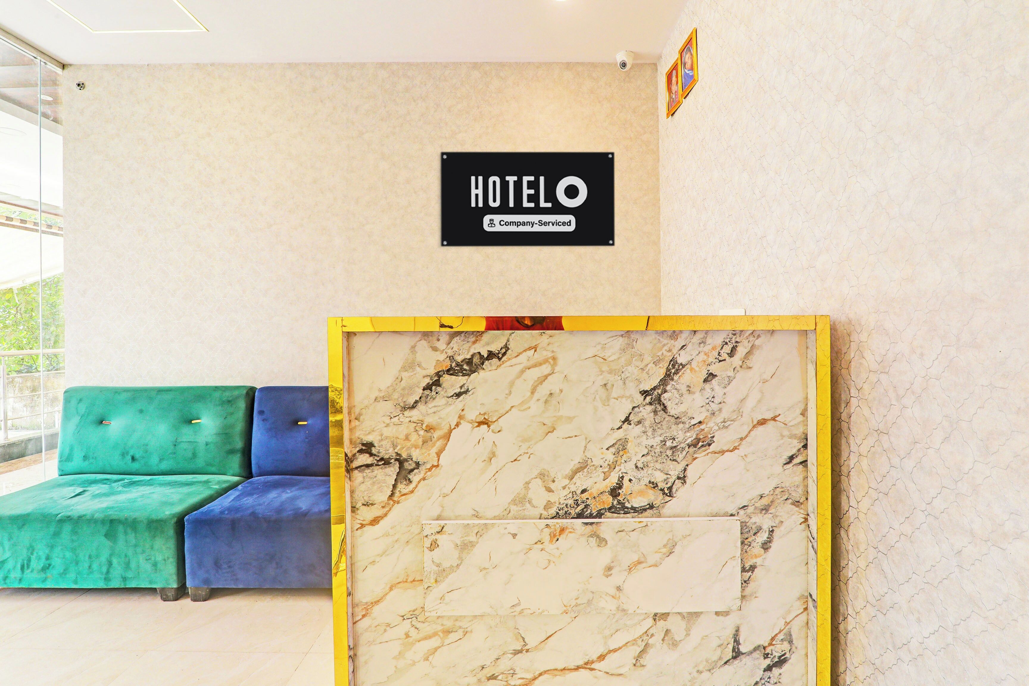 Zona de recepción de un hotel con pared de mármol, cartel que indica que es un hotel de servicios corporativos y una sala de espera con sofás tapizados en tonos verde y azul.