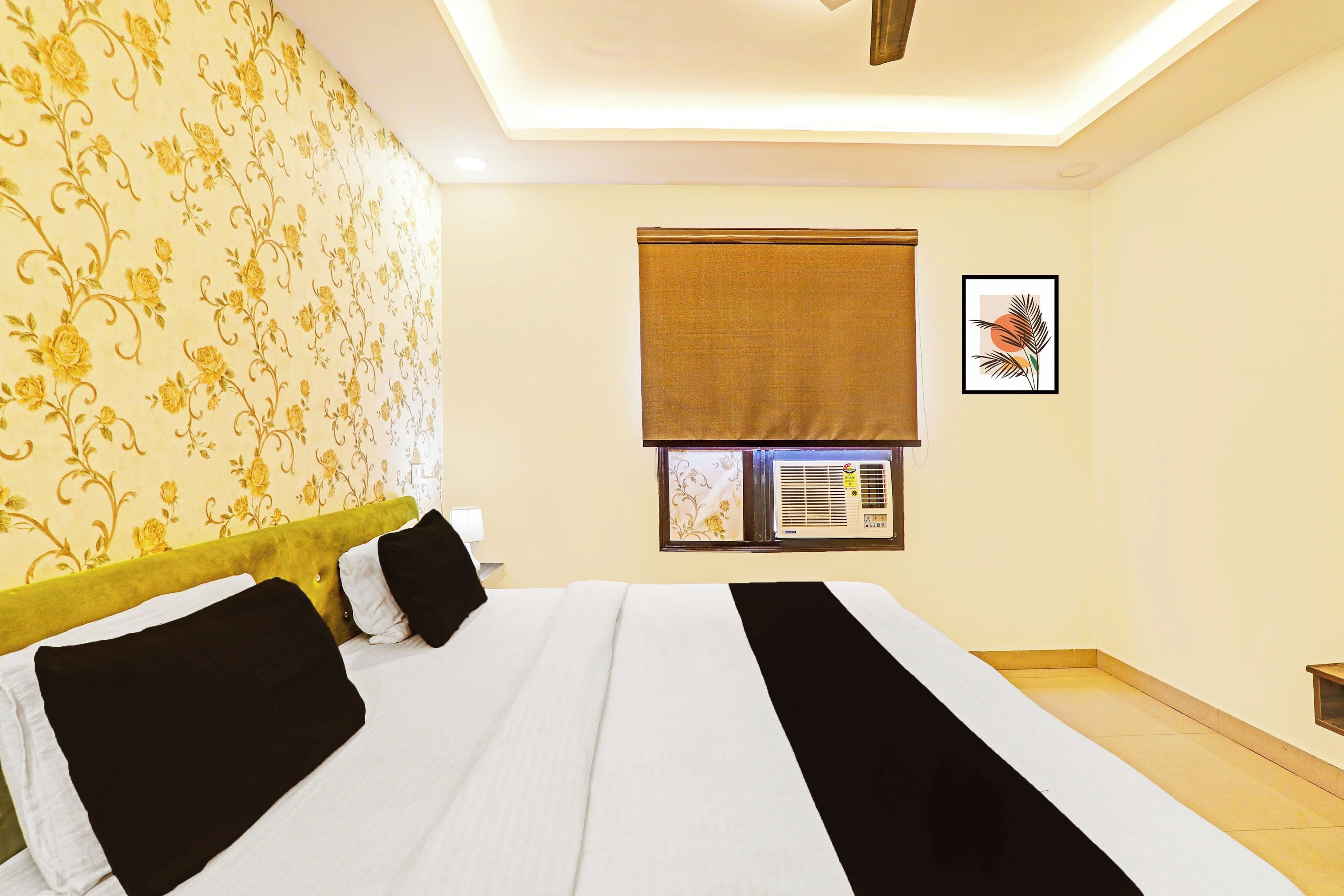 Habitación de hotel con cama, ventana con persiana, aire acondicionado de pared y un cuadro enmarcado.