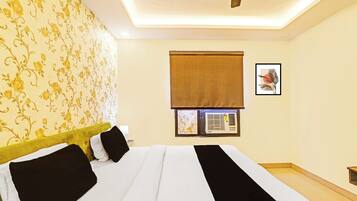 Habitación de hotel con cama, ventana con persiana, aire acondicionado de pared y un cuadro enmarcado.