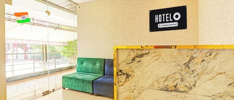 A hotel reception area with a marble reception desk, a green and blue sofa, and a sign indicating the hotel is company-serviced.