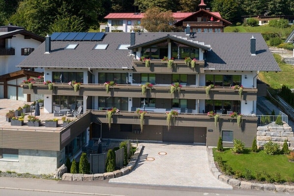 Um hotel de vários andares com design moderno, apresentando varandas com plantas, entrada pavimentada e área ajardinada ao redor.