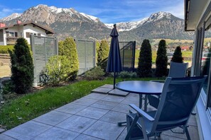 Um pátio com mesa e cadeiras, um pequeno guarda-sol e vista para montanhas cobertas de neve.