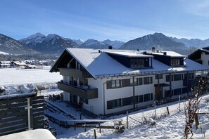 Um edifício moderno com telhado inclinado, janelas amplas e vista para montanhas cobertas de neve.