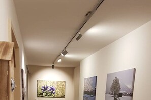 Ein Korridor mit Kunstwerken an den Wänden, einer Deckenleuchte und einer Tür links.