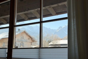 A room with large windows offering a view of mountains and a wooden building. - Holiday apartment with 1 bedroom (Garmisch-Partenkirchen)