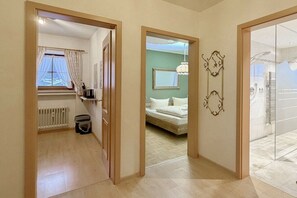 A hotel room with a bed, a radiator, a window with curtains, and a hallway leading to another room. - Holiday apartment with 1 bedroom (Garmisch-Partenkirchen)