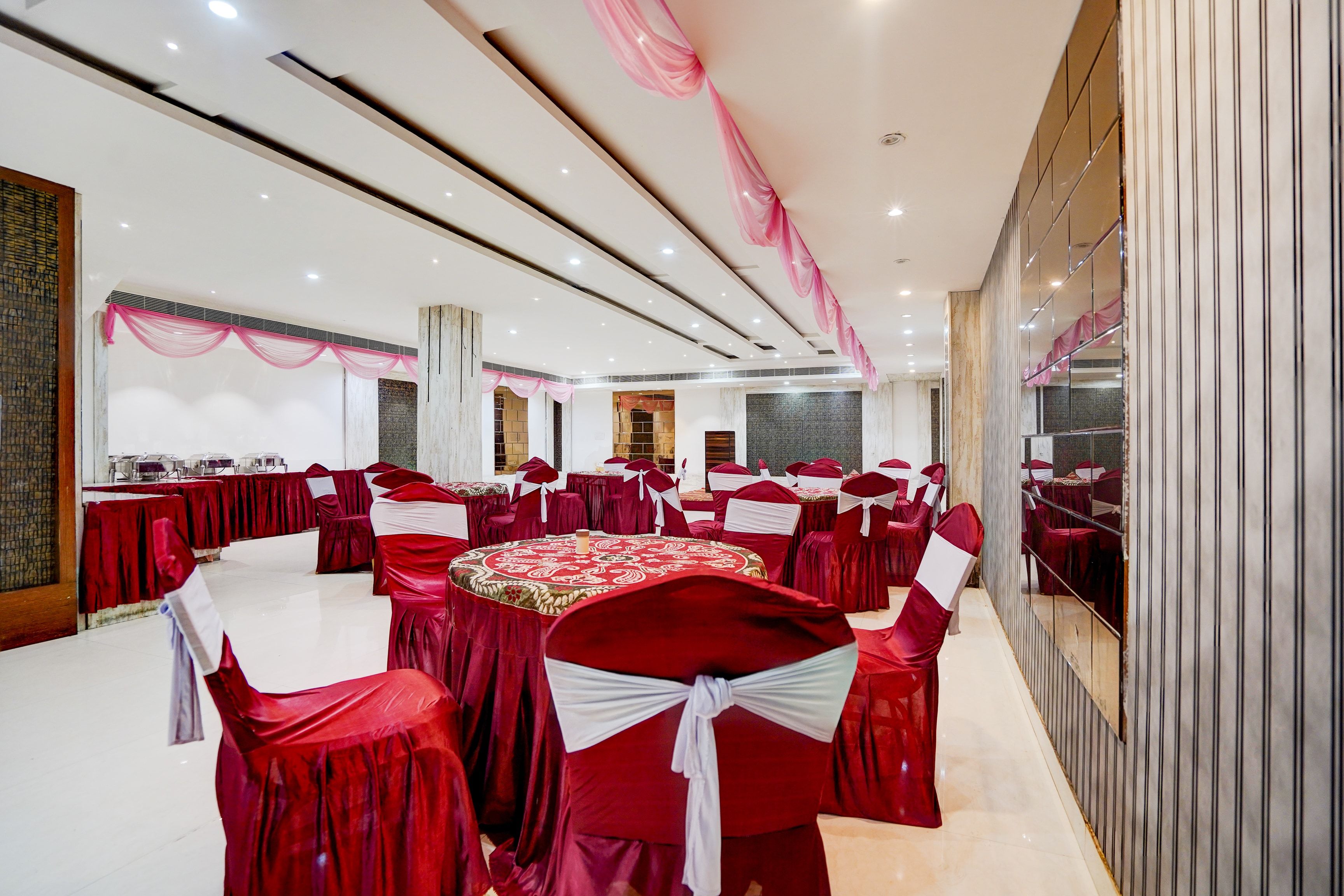 A banquet hall with round tables, red tablecloths, and chairs with white sashes.