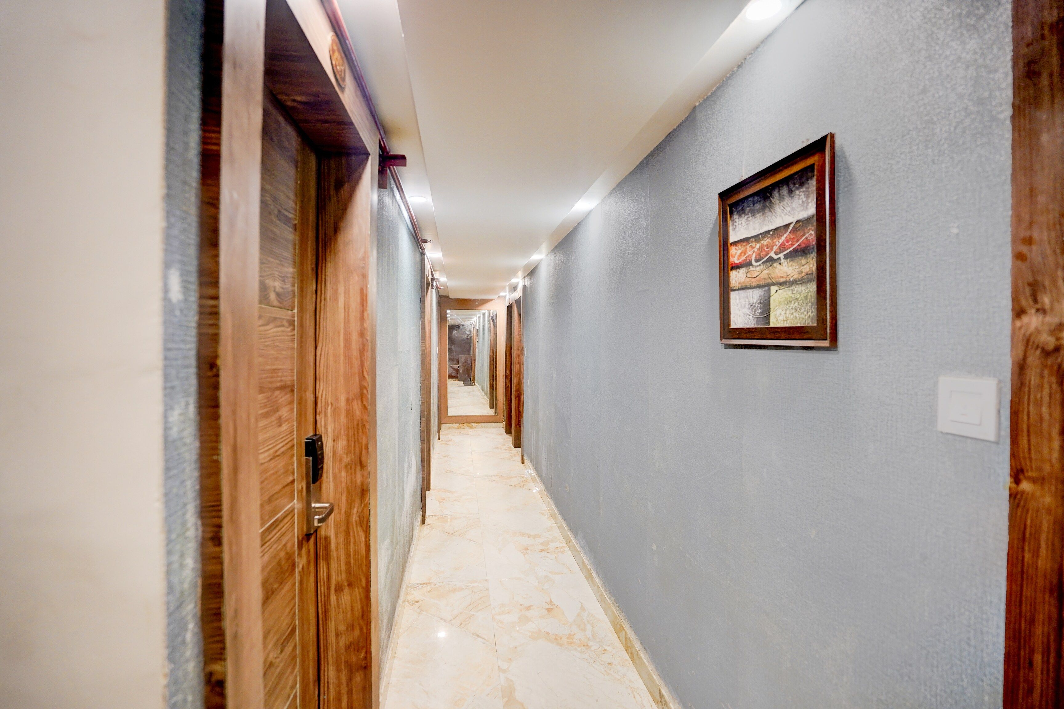 A corridor with wooden doors, a marble floor, and a framed artwork on the wall.