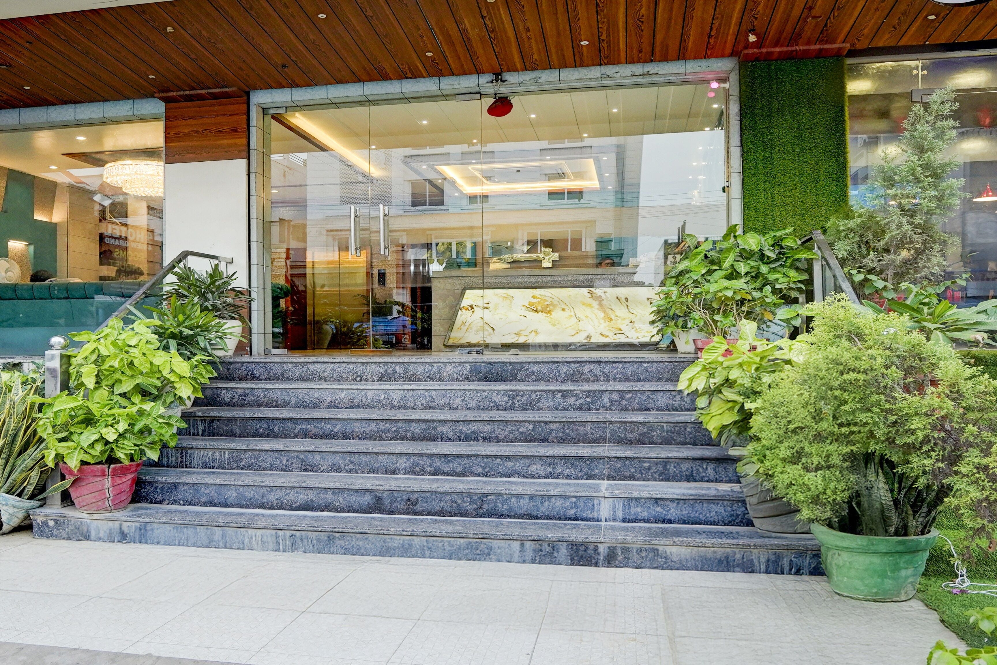 A hotel entrance with a glass facade, a staircase leading to the entrance, and potted plants around the steps.