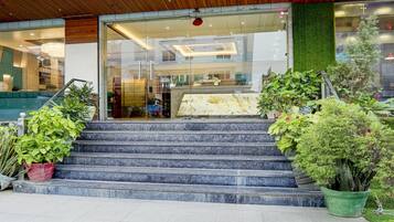 A hotel entrance with a glass facade, a staircase leading to the entrance, and potted plants around the steps.