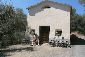 A small building with a single door and a window, a bicycle parked in front, and a person sitting on a bench. - Holiday home with 3 bedrooms (Pietrabruna)
