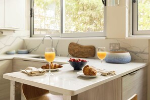 A breakfast setting with croissants, a bowl of strawberries, and glasses of orange juice on a kitchen counter. - Kensington 2-Bed near Notting Hill with Garden (London)