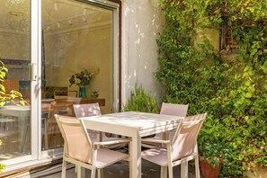 Eine Terrasse im Freien mit Tisch und Stühlen, umgeben von Pflanzen und einer Glastür.
